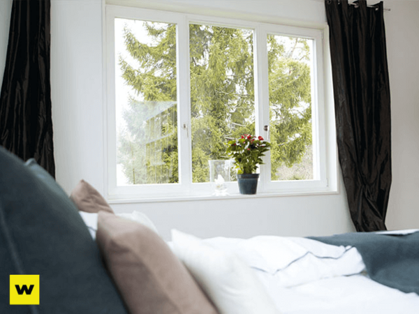 Helles Schlafzimmer mit großem Fenster, Zimmerpflanze und Blick ins Grüne für Wohnkomfort.