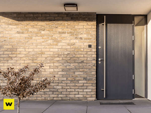 Moderne Haustür vor heller Klinkerfassade mit kleiner Pflanze und sauberem Eingangsbereich.